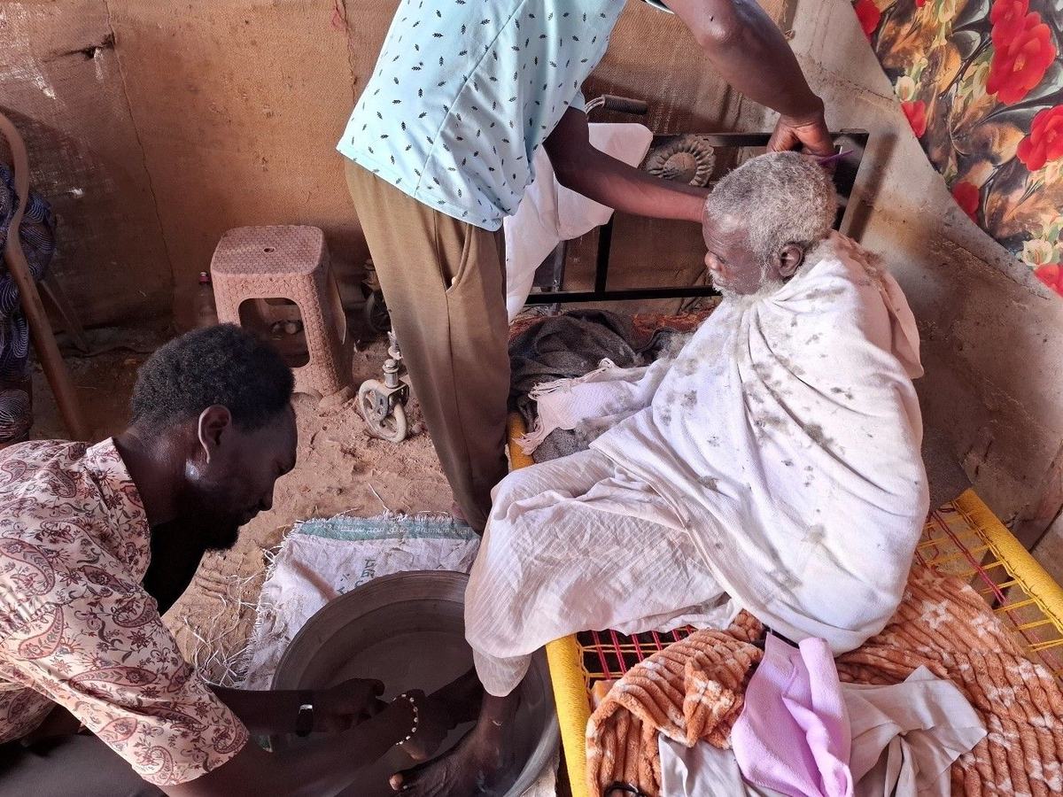Volunteers assist an older man with hair and nail care.